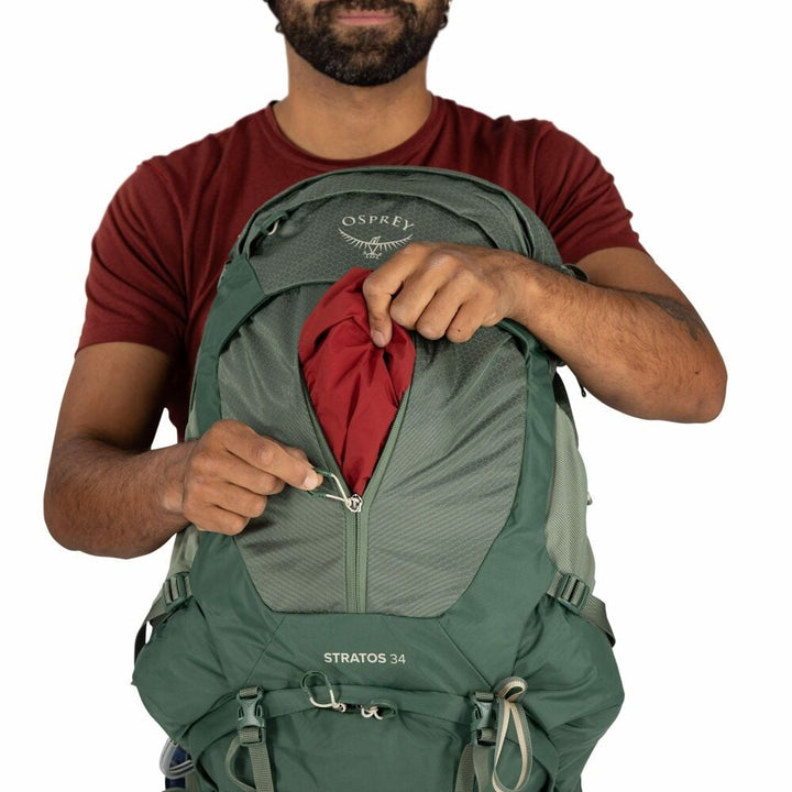 Person packing a green Osprey backpack on a white background
