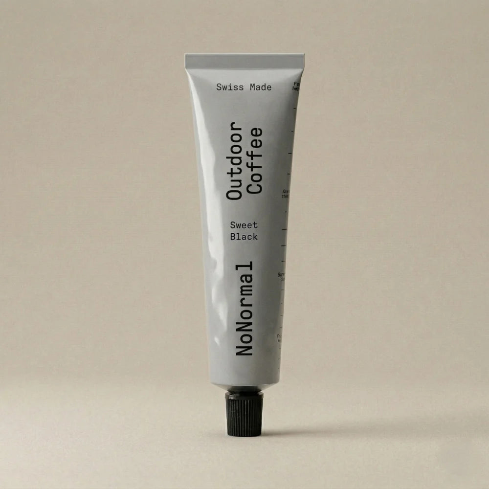 A light gray squeeze tube of NoNormal Outdoor Coffee Sweet Black, standing upright on a matching light beige background.