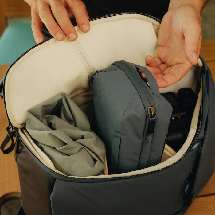 Person opening a black backpack to reveal a gray bag inside on a wooden surface.
