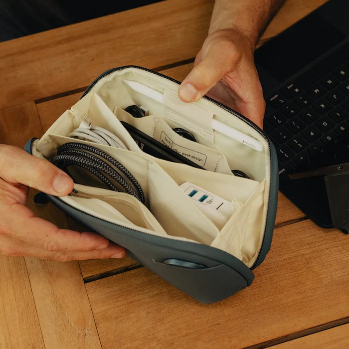Person holding open accessory pouch filled with different tech devices on a wooden counter