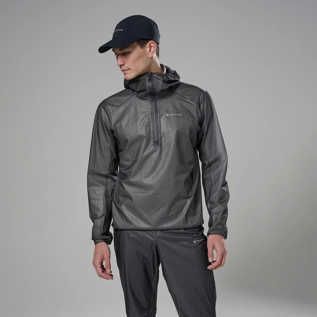 Man wearing a gray rain jacket and pants with a black cap on a gray background