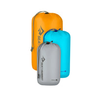Three Sea to Summit compression bags in orange, gray, and blue on a white background