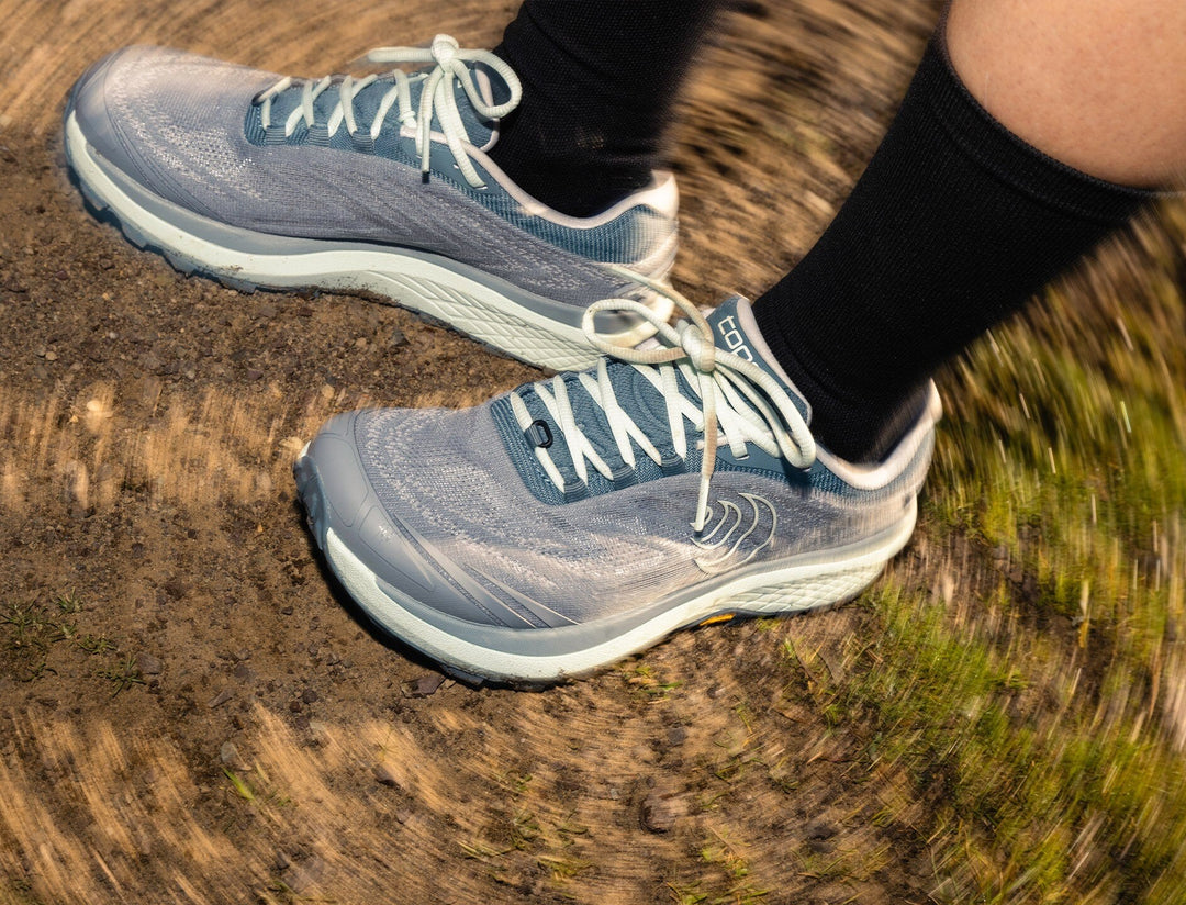 Person wearing grey and mint running shoes on a dirt track, close up on shoes