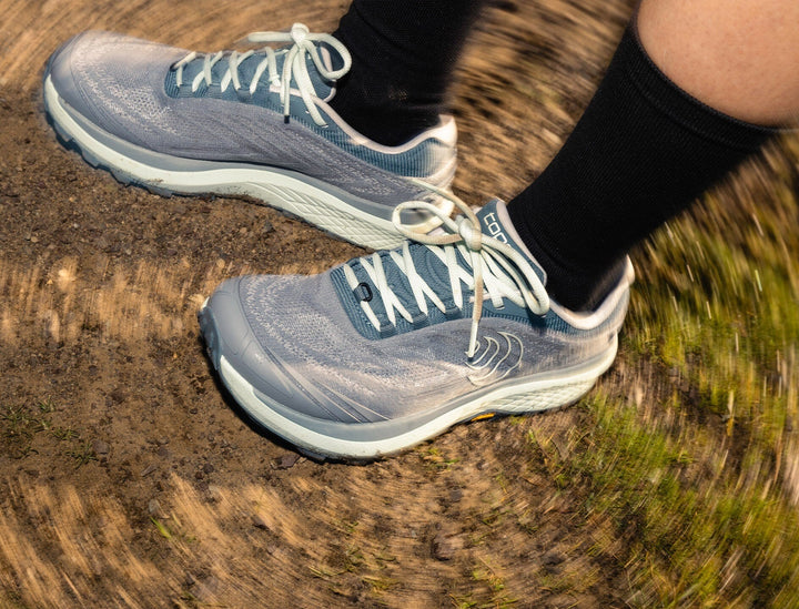 Person wearing grey and mint running shoes on a dirt track, close up on shoes
