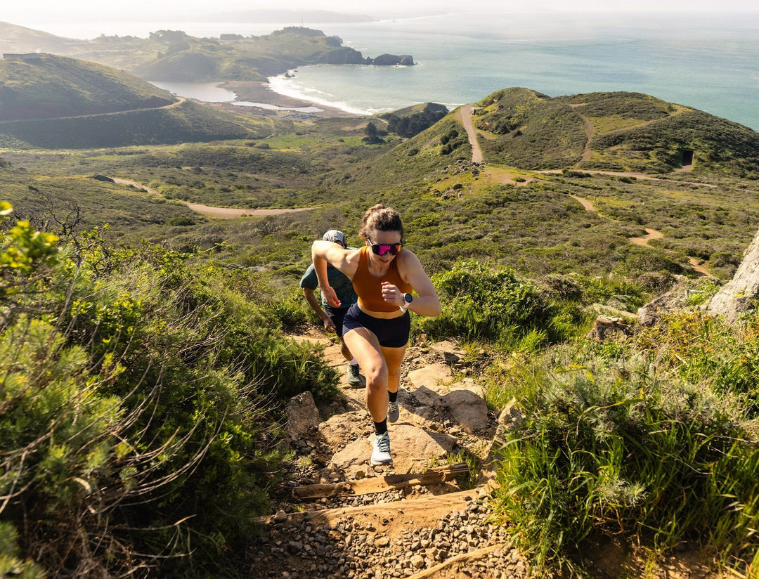 Two people running on a rough trail with a scenic coastal background