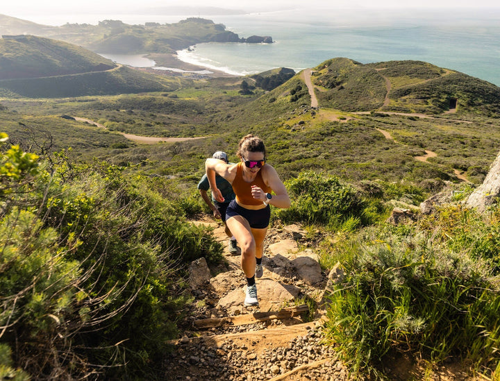 Two people running on a rough trail with a scenic coastal background