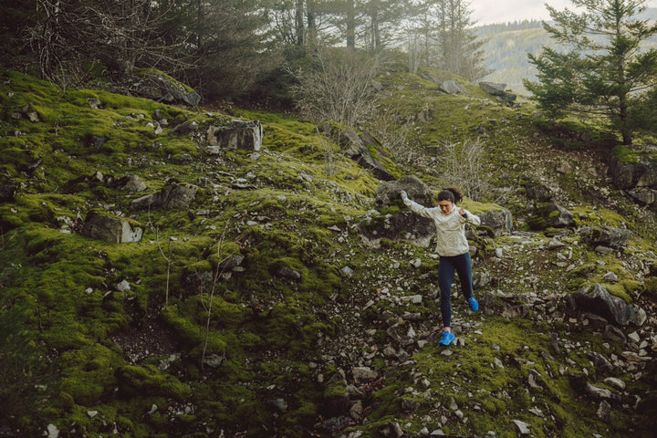 Person runs down rocky hillside wearing blue running shoes
