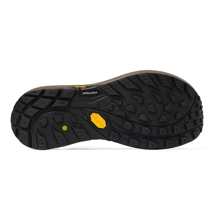 The treaded black rubber outsole of a hiking boot, featuring a yellow Vibram logo and a small green reflector, shown against a white background.