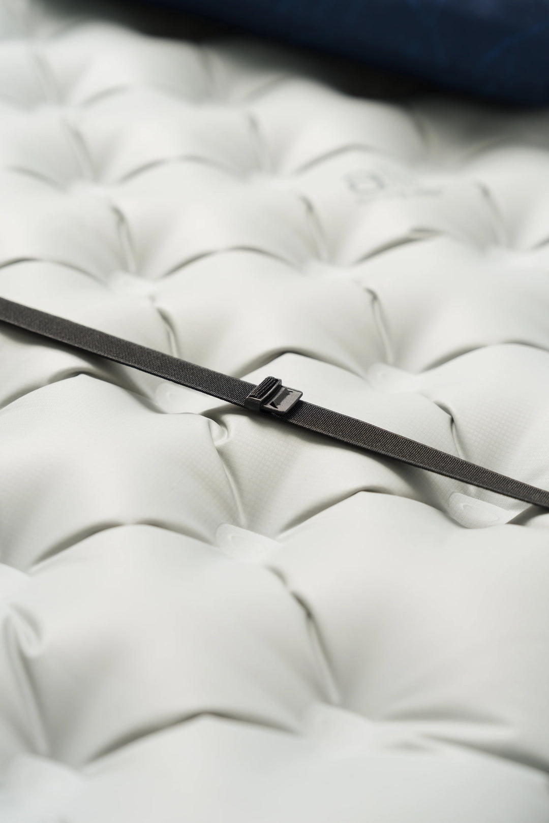 A close-up of a black strap or band with a small metal buckle resting diagonally across a white tufted surface.