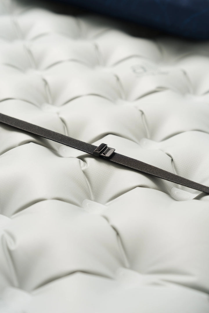 A close-up of a black strap or band with a small metal buckle resting diagonally across a white tufted surface.