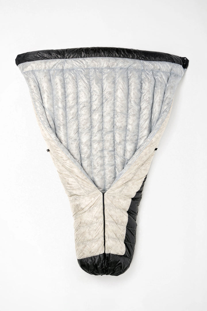 A light gray and off-white puffer sleeping bag with black trim, shown laid flat against a white background.