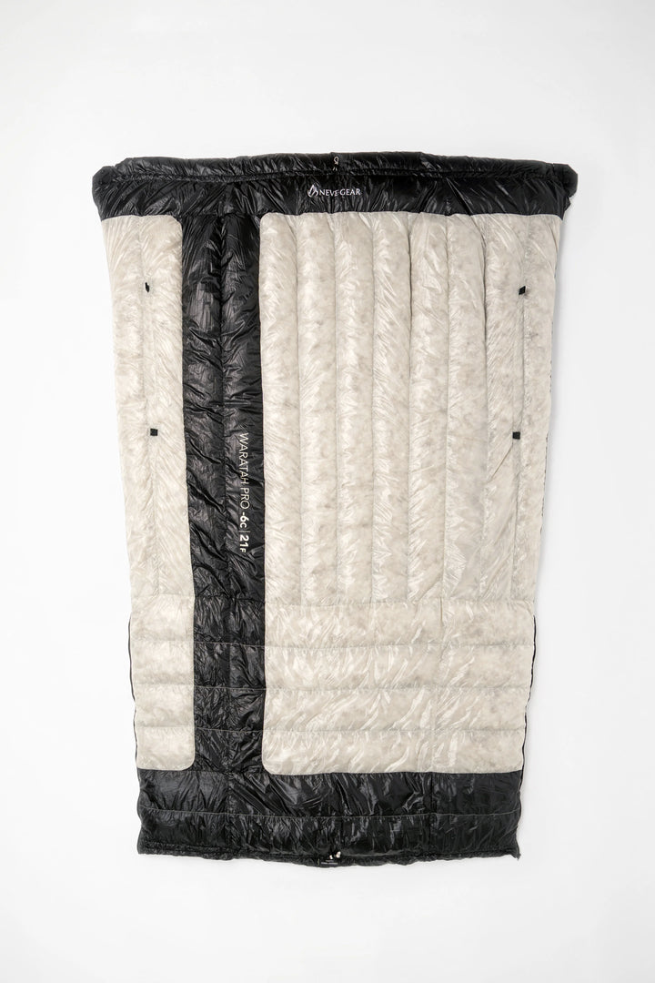A folded sleeping bag or padded mat shown flat against a plain white background. The product has a light beige quilted outer panel with a vertical black center stripe and black top/bottom trim.