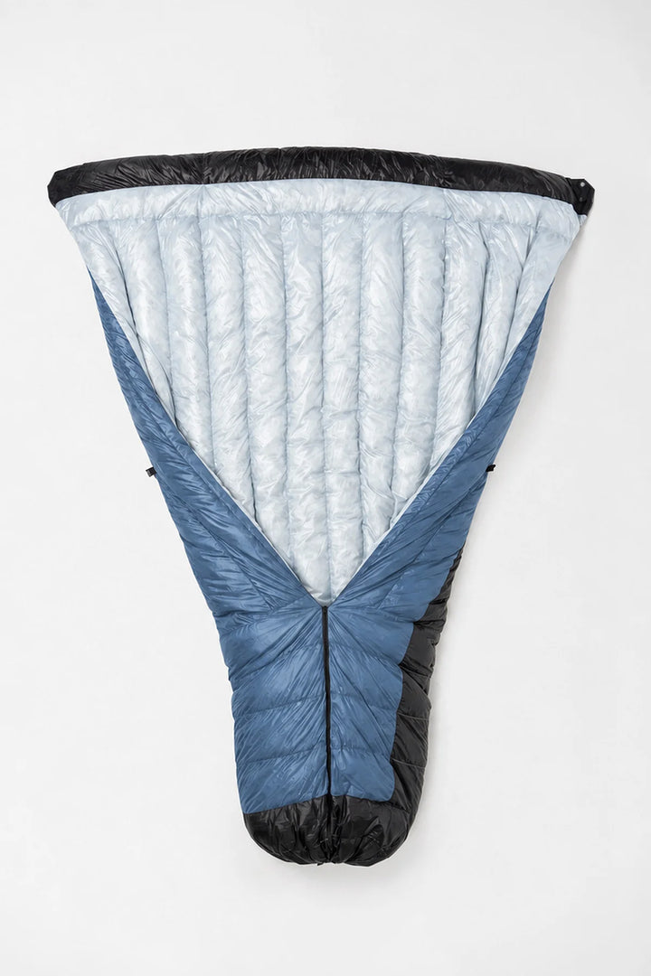 A technical insulated sleeping bag shown flat against a plain white background, featuring a light blue quilted shell, slate blue body panels, and black trim.
