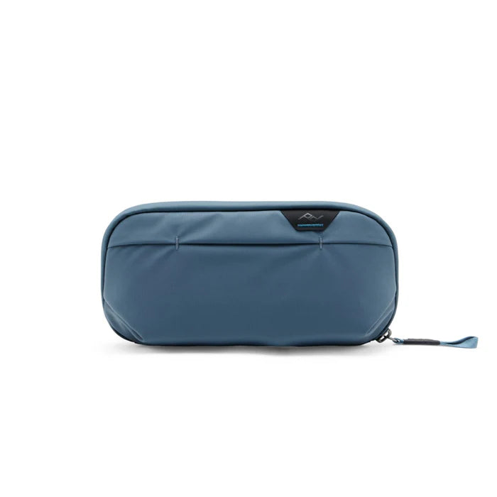 A slate blue zippered pouch with a small black brand tab on the front, shown against a plain white background.