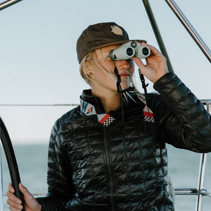 Person on a boat looking through binoculars while wearing a floral patterned camera strap