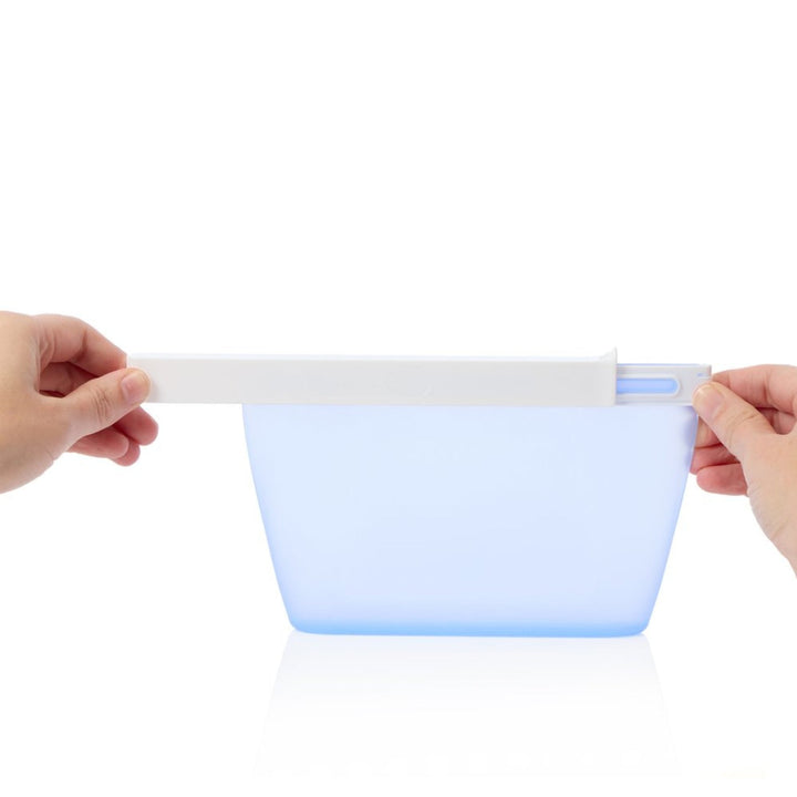 Collapsible blue silicone bag held by two hands on a white background