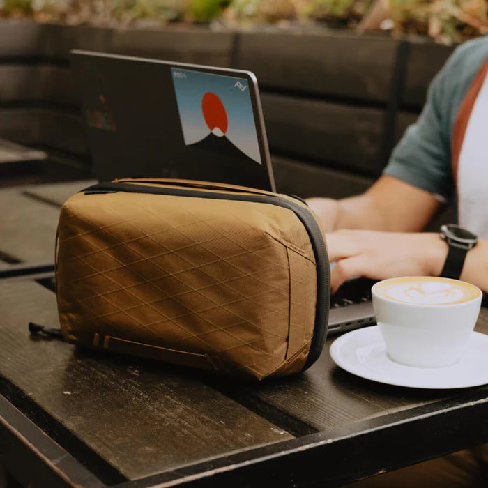Person using a laptop with a brown quilted bag on a table next to a cup of coffee.