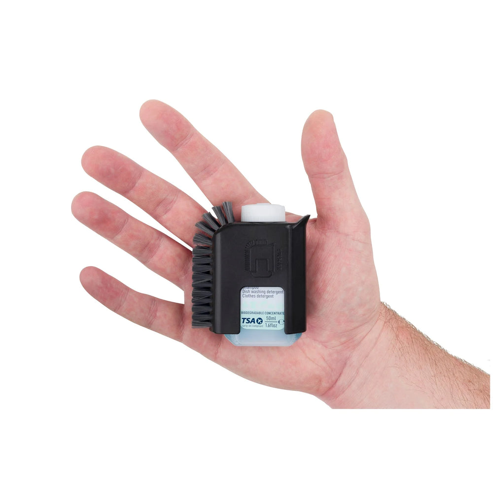 Black scrubbing brush containing a bottle of detergent held in the palm of a hand