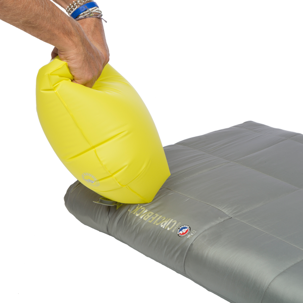 Person using yellow pump sack to inflate grey sleeping mat.