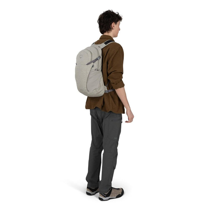 A man shown from the back wearing a light gray backpack, a brown shirt, and dark gray pants against a plain white background.