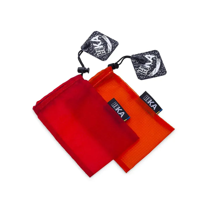 Two small drawstring pouches, one red and one orange, with black LELEKA brand tags and two matching black square patches, shown on a plain white background.