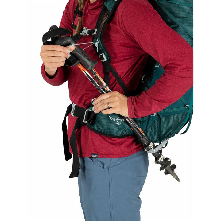 Person wearing a red jacket and teal backpack with hiking poles on a white background