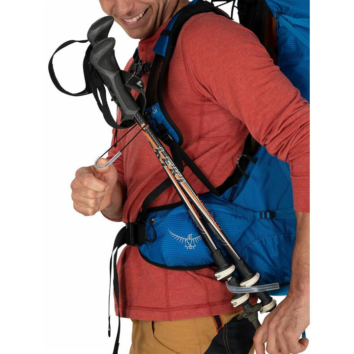 Person with a blue backpack holding hiking poles on a white background