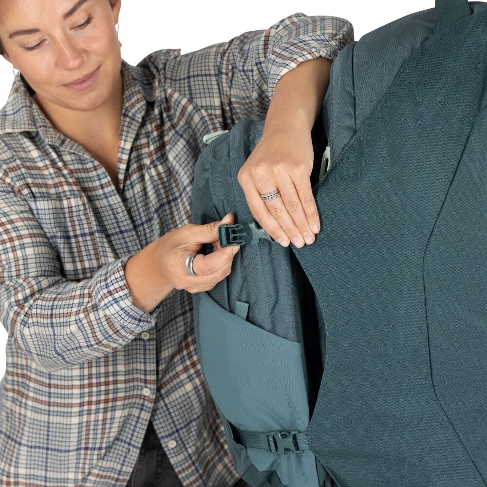 Person adjusting a teal backpack with a white background