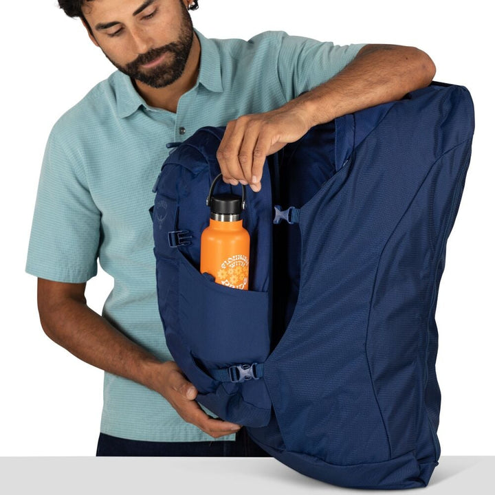 Man placing an orange water bottle into a blue backpack on a white background