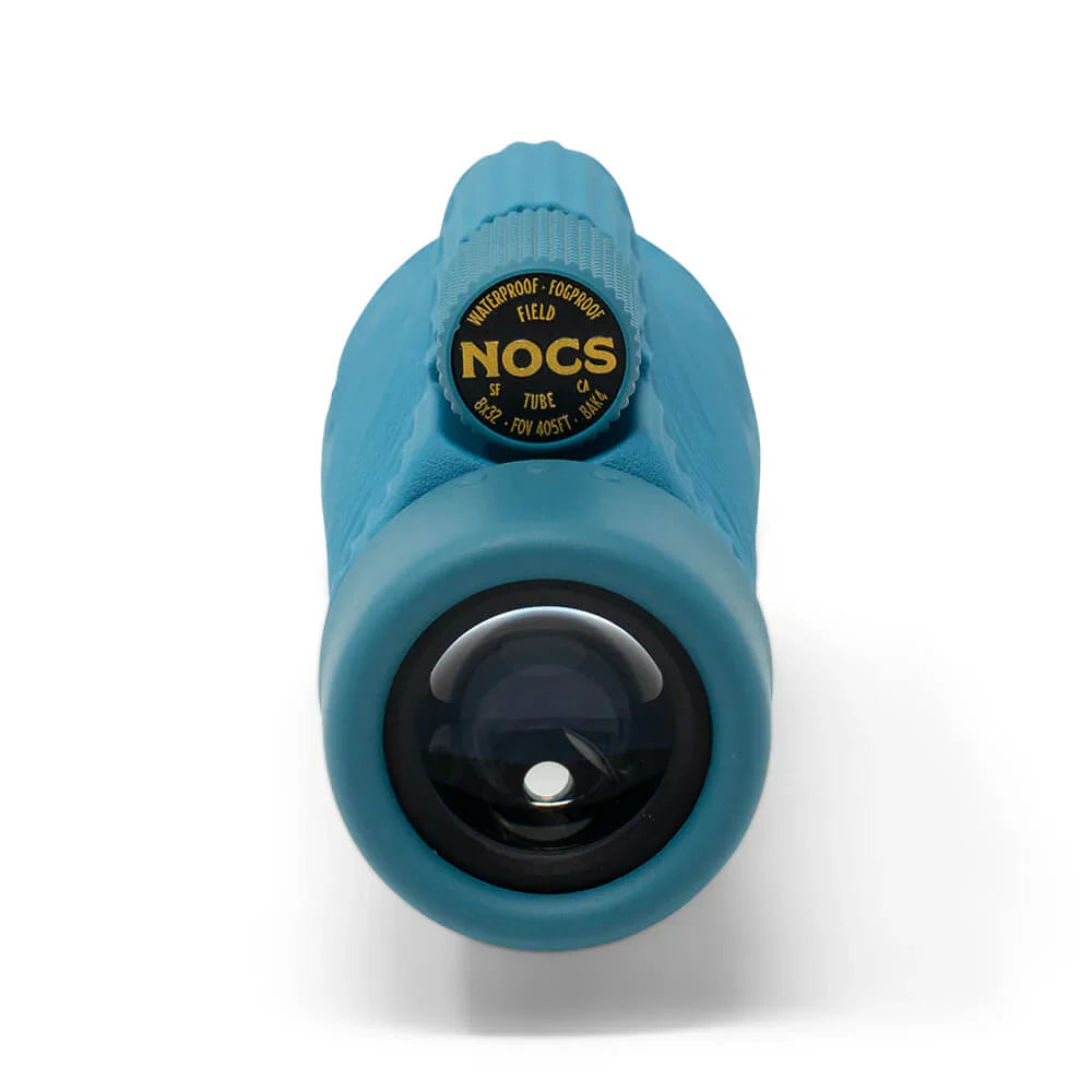 A close-up shot of a teal blue NOCS waterproof tube lens with a black and gold label on a white background.