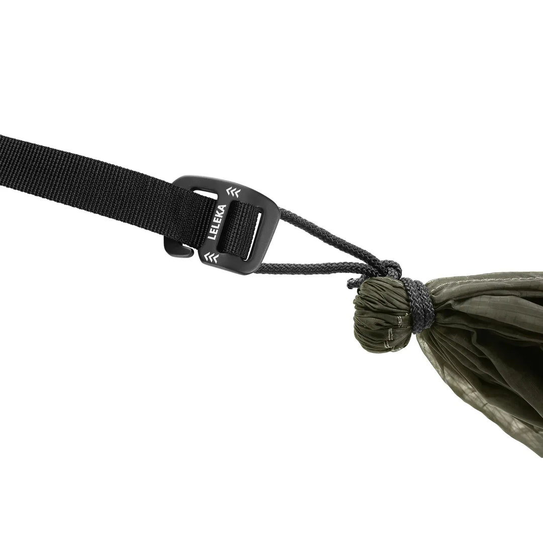 Close-up of a black webbing strap with a black plastic buckle and a dark cord tied to an olive green fabric loop, on a white background. The buckle shows the LELEKA brand name.