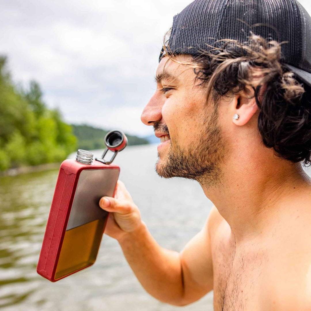 Man holding a red flask by a lake
