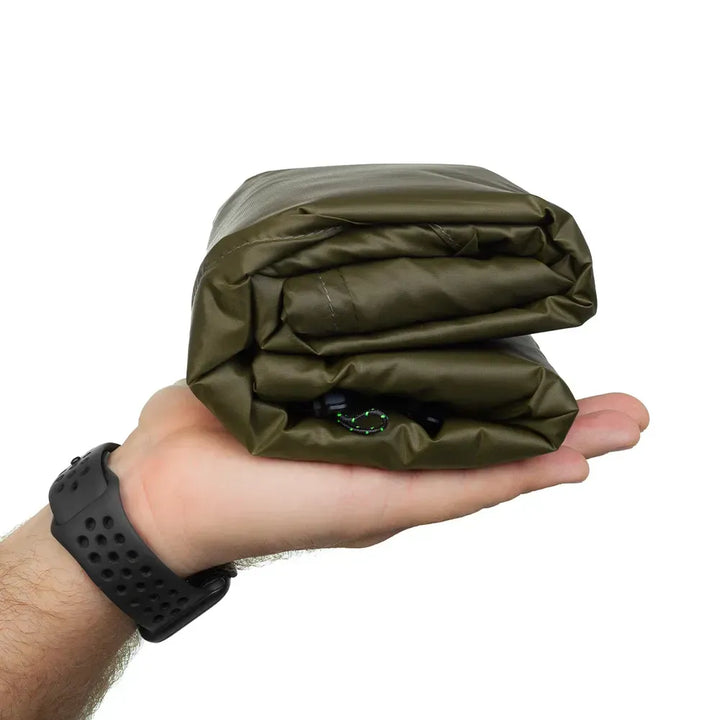 A hand holding a folded olive green tarp against a plain white background.