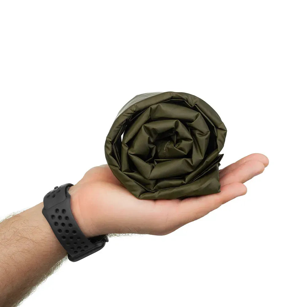 An olive green rolled tarp held in a person's hand, with a black perforated wristwatch visible on the wrist, against a plain white background.