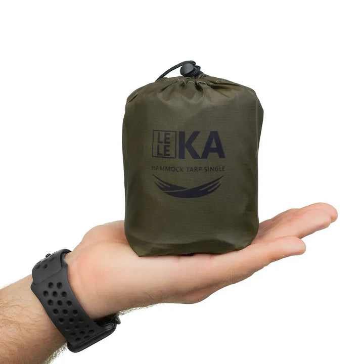 Small green hammock tarp single in a drawstring bag held in a hand on a white background