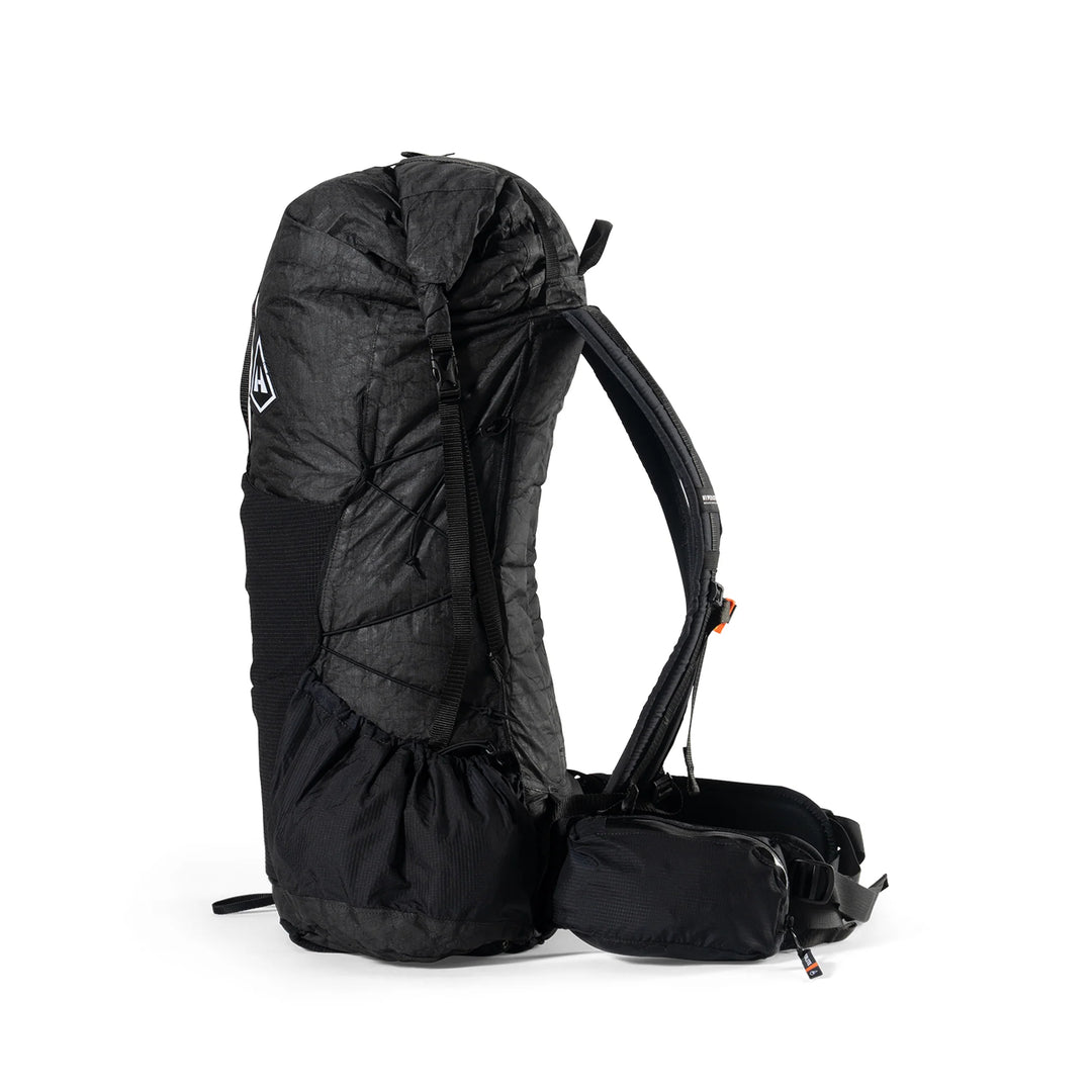 A black technical backpack shown from the side against a plain white background, featuring a padded upper section, compression straps, and a small attached pouch.