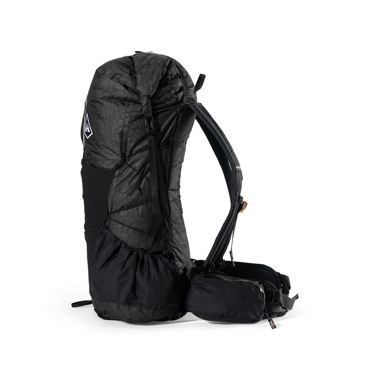 A black technical backpack shown from the side against a plain white background, featuring a padded upper section, compression straps, and a small attached pouch.