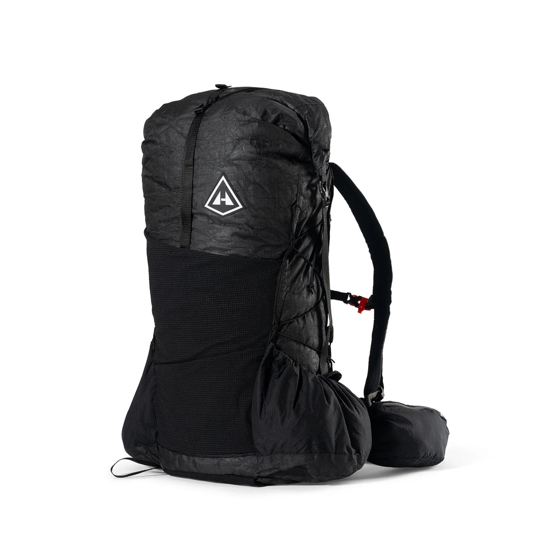 A black technical backpack shown from the side against a plain white background, featuring a white triangular logo on the upper section.