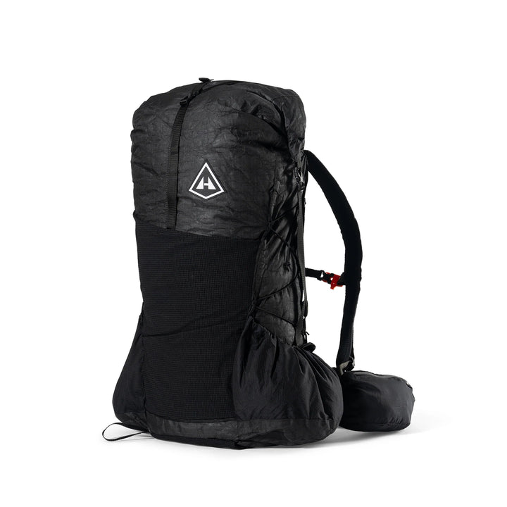 A black technical backpack shown from the side against a plain white background, featuring a white triangular logo on the upper section.
