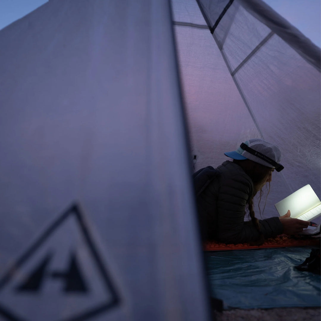 Person reading a book inside a tent with a visible brand logo.