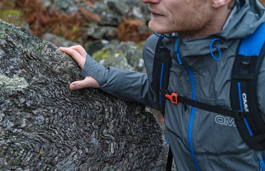 Person wearing a gray waterproof jacket with blue accents, standing next to a textured rock surface.
