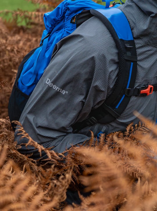Person wearing a gray waterproof jacket featuring the Dyneema logo on the shoulder moving through bracken.