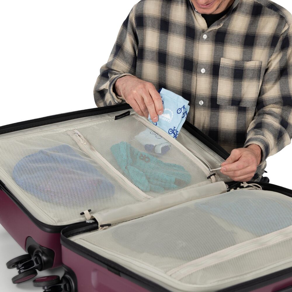 Person packing a suitcase with travel items on a white background