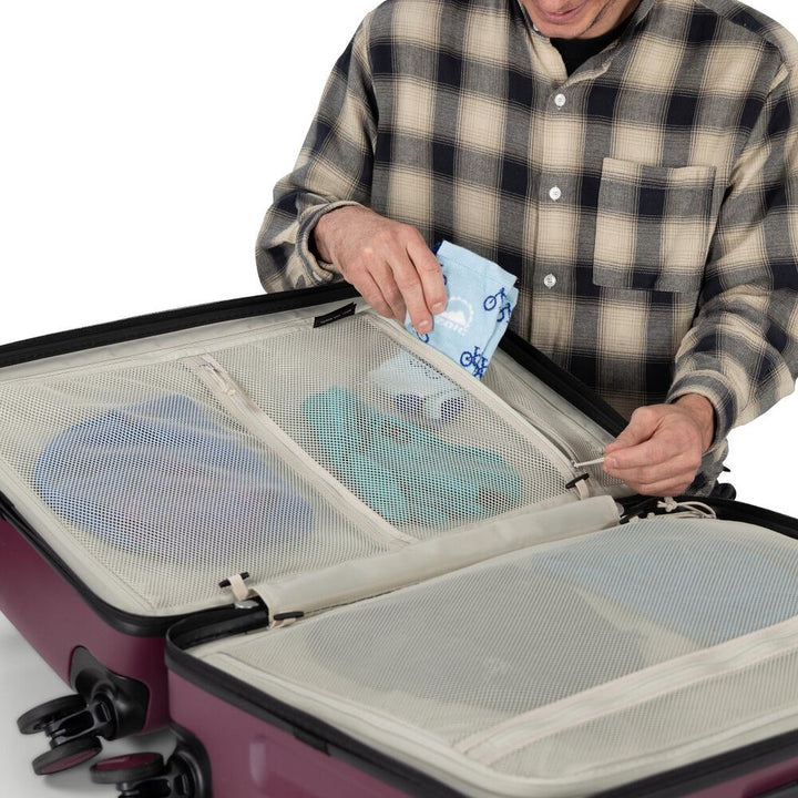 Person packing a suitcase with travel items on a white background
