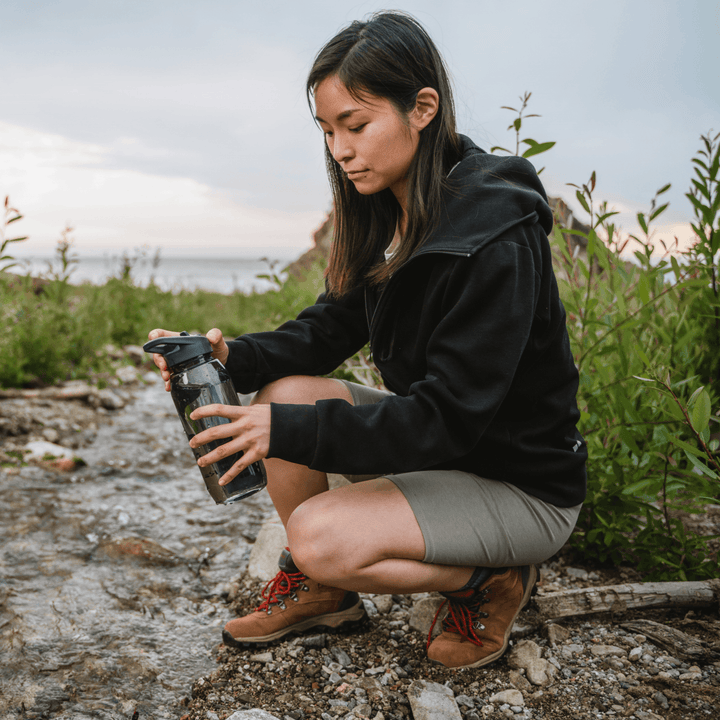 Person fills a water bottle from a gravelly stream