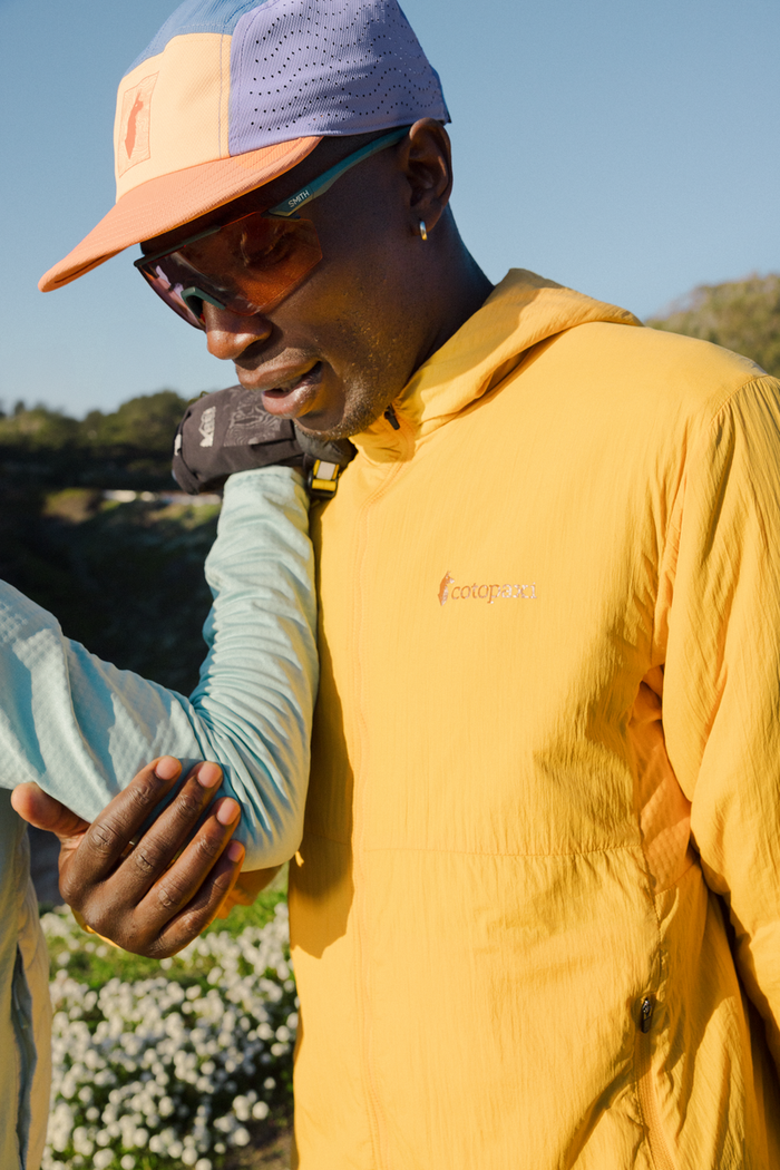 Person wearing a yellow jacket with a brand logo, standing outdoors with a clear sky.
