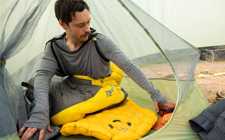 Person sitting inside a tent with yellow sleeping pad