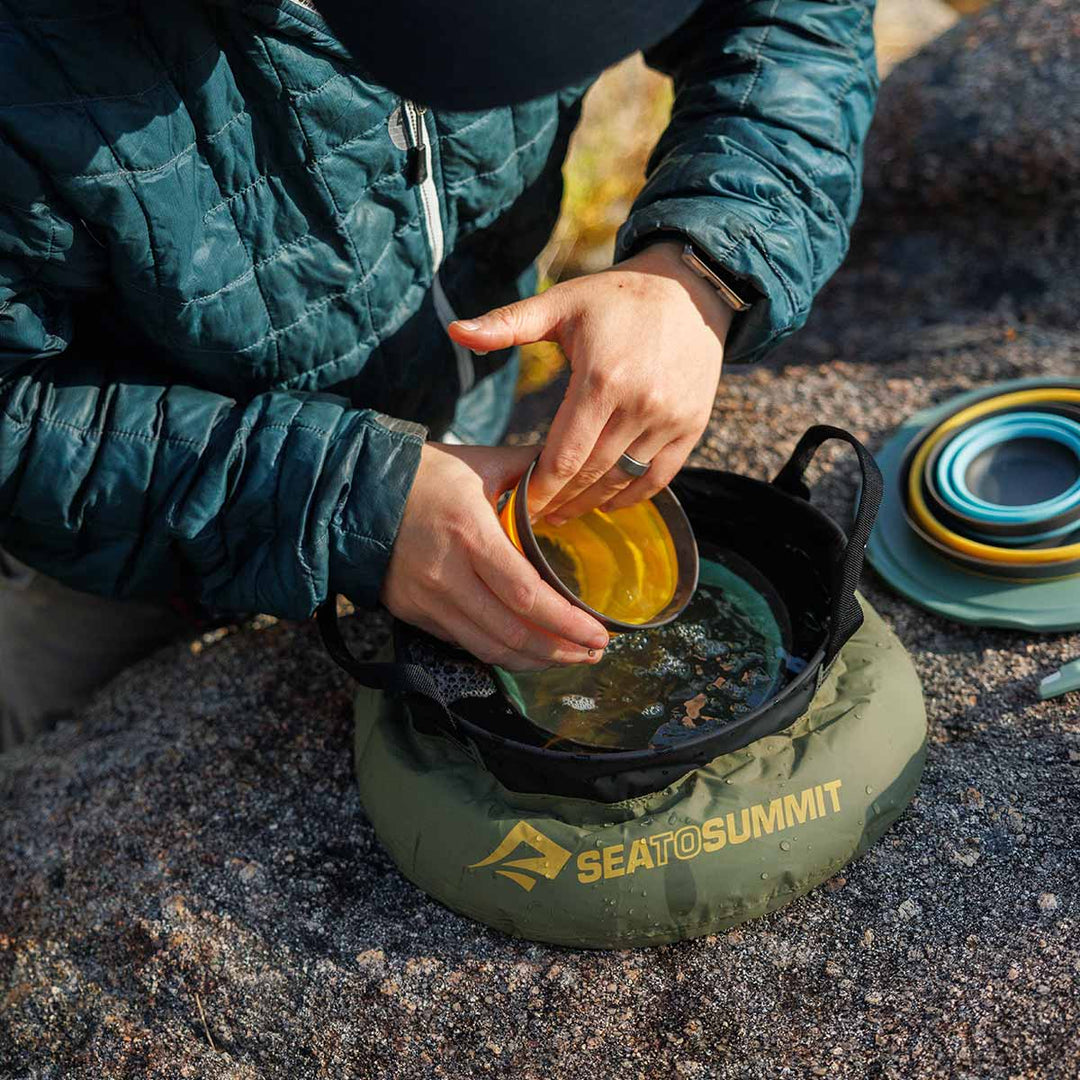 Person using a Sea to summit camping sink on a rocky surface