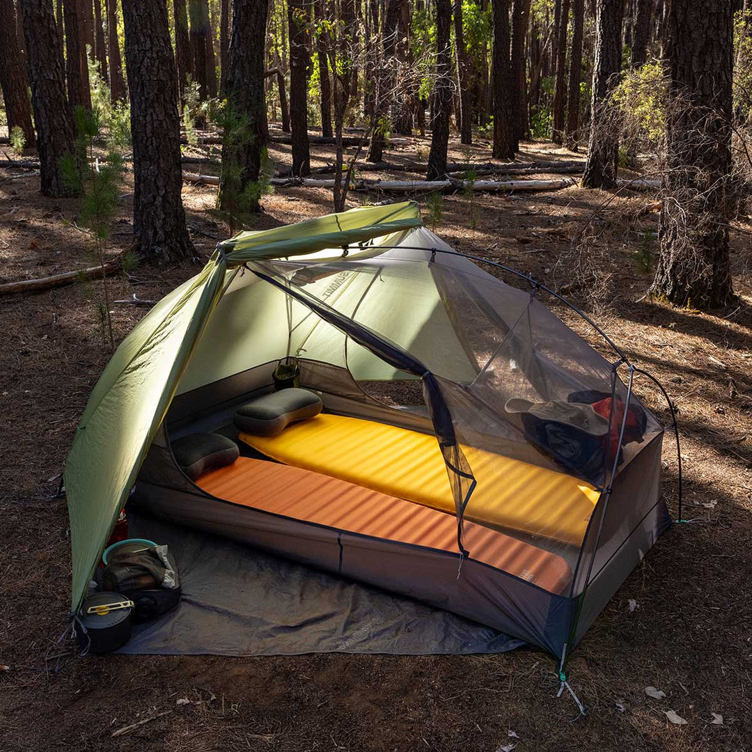 Green hiking tent with fly rolled half back to reveal one orange and one yellow sleeping mat set up inside.