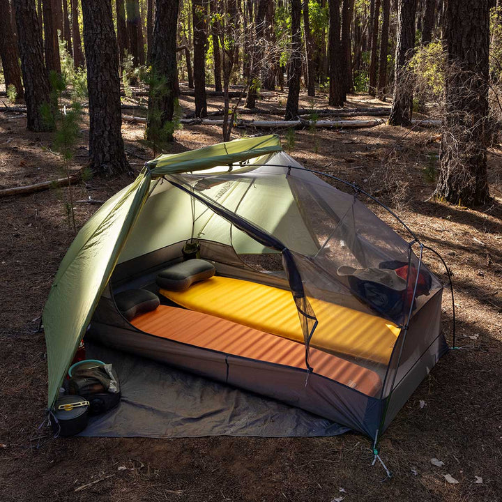 Green hiking tent with fly rolled half back to reveal one orange and one yellow sleeping mat set up inside.